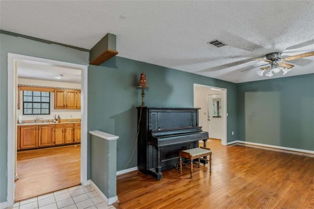 miscellaneous room featuring a textured ceiling, ceiling fan, light wood-type flooring, and sink