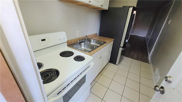 kitchen with light tile patterned flooring, white electric range, stainless steel refrigerator, white cabinetry, and sink