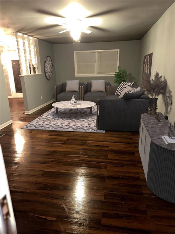 living area with baseboards, dark wood-type flooring, and ceiling fan