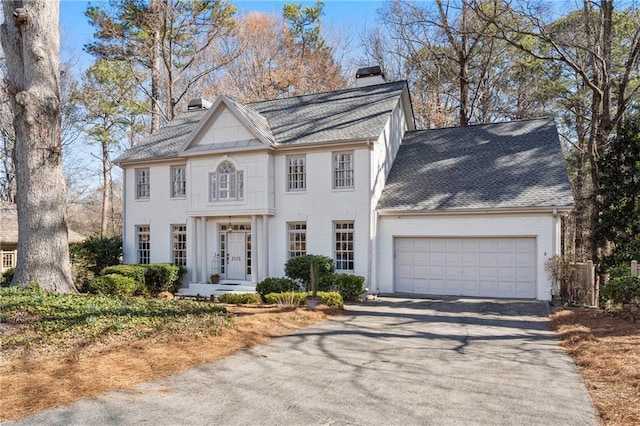 view of front facade featuring brick siding, a chimney, a shingled roof, a garage, and driveway