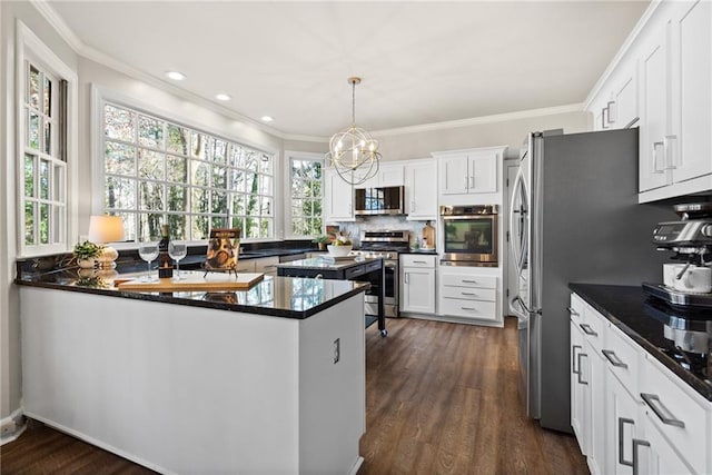 kitchen with appliances with stainless steel finishes, hanging light fixtures, white cabinets, and kitchen peninsula