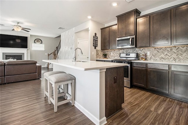 kitchen with sink, stainless steel appliances, dark brown cabinetry, tasteful backsplash, and an island with sink