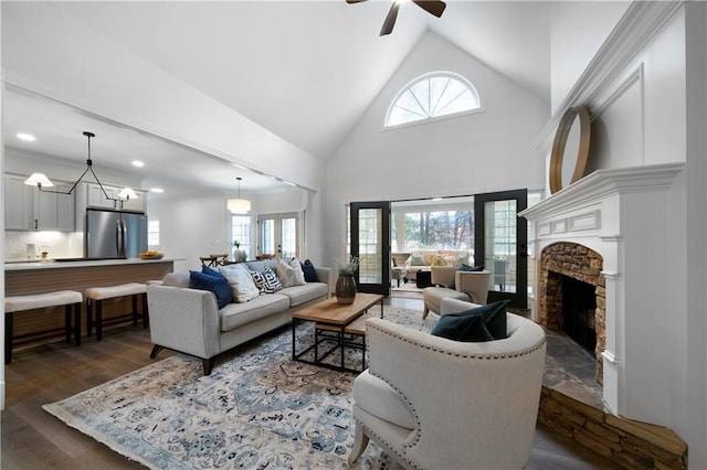 living area with dark wood-type flooring, a healthy amount of sunlight, high vaulted ceiling, and a stone fireplace