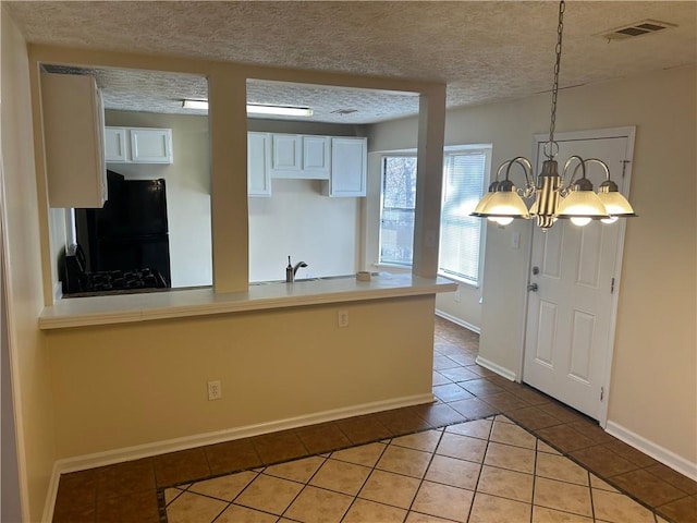 kitchen with black fridge, white cabinetry, a textured ceiling, hanging light fixtures, and light tile patterned floors