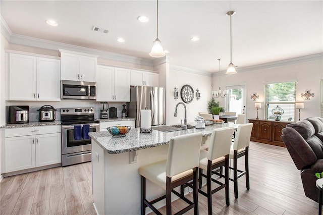 kitchen featuring white cabinetry, appliances with stainless steel finishes, a kitchen island with sink, and hanging light fixtures