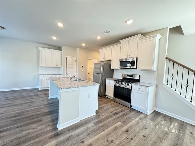 kitchen featuring white cabinets, a center island with sink, appliances with stainless steel finishes, light stone countertops, and light wood-type flooring