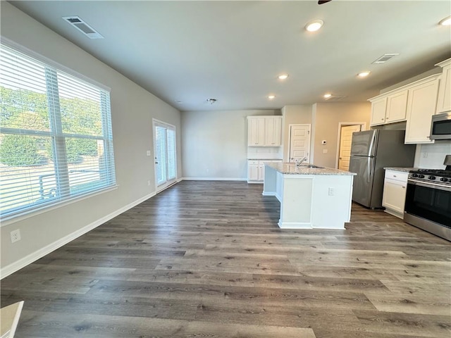 kitchen with appliances with stainless steel finishes, white cabinets, hardwood / wood-style floors, and a kitchen island with sink