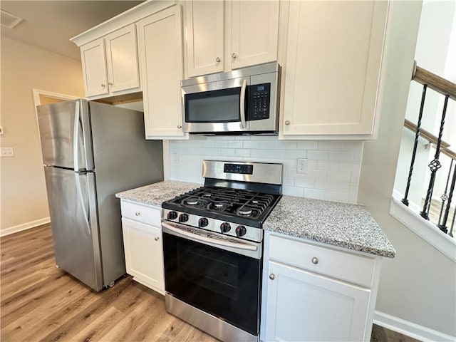 kitchen featuring white cabinets, backsplash, appliances with stainless steel finishes, light stone countertops, and light wood-type flooring