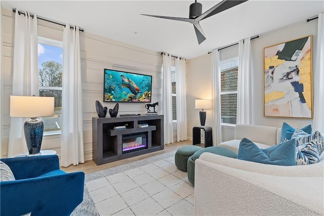 living area featuring light tile patterned floors, plenty of natural light, a ceiling fan, and a glass covered fireplace