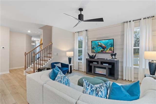 living area with baseboards, a ceiling fan, a glass covered fireplace, stairway, and wood finished floors