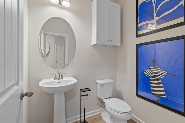 half bathroom with baseboards, a sink, toilet, and wood finished floors