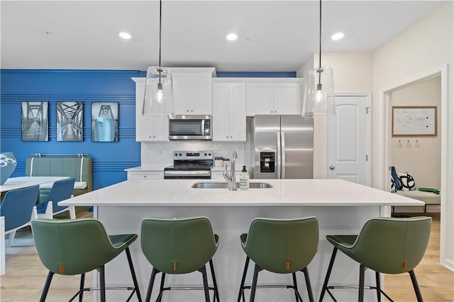 kitchen featuring stainless steel appliances, a breakfast bar, a sink, white cabinets, and backsplash