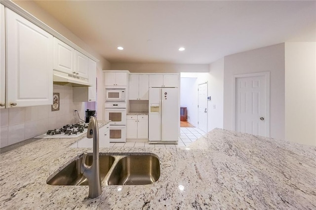 kitchen featuring white appliances, sink, light stone countertops, tasteful backsplash, and white cabinetry