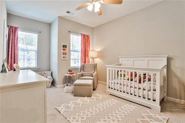 carpeted bedroom featuring ceiling fan and a crib