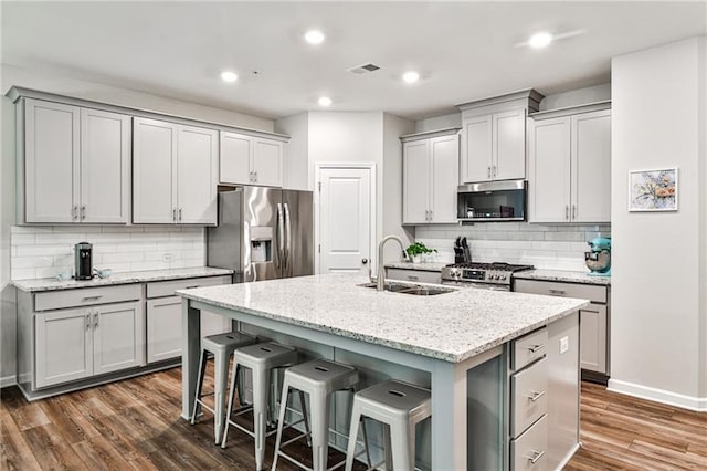 kitchen featuring sink, a kitchen island with sink, light stone countertops, a breakfast bar area, and stainless steel appliances