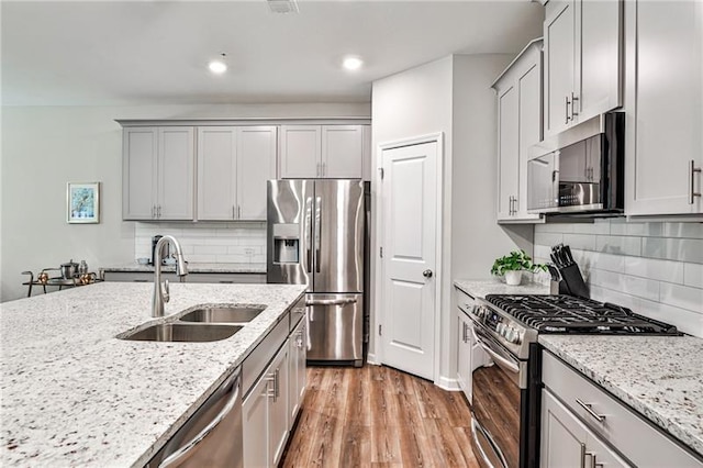 kitchen featuring backsplash, appliances with stainless steel finishes, sink, and light stone counters