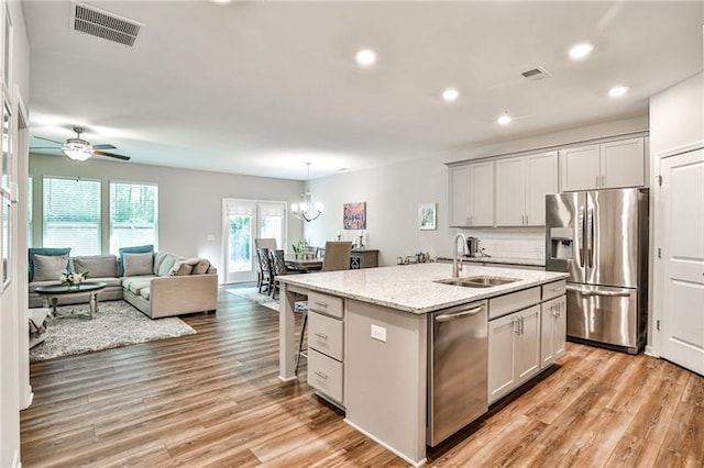 kitchen featuring sink, a kitchen island with sink, light stone countertops, appliances with stainless steel finishes, and ceiling fan with notable chandelier