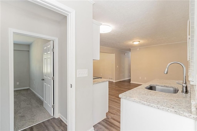 kitchen with light stone counters, dark carpet, sink, and white cabinetry