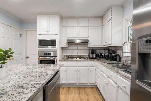 7275 Oswego Trl, Riverdale, GA 30296 - kitchen with tasteful backsplash, white cabinets, under cabinet range hood, light wood-style floors, and appliances with stainless steel finishes