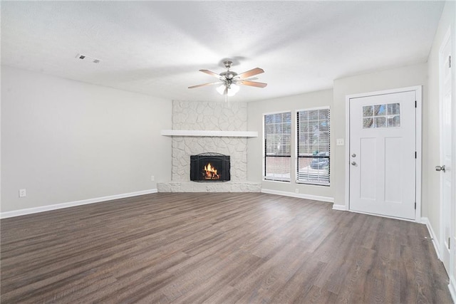 unfurnished living room featuring ceiling fan, dark hardwood / wood-style floors, a stone fireplace, and a textured ceiling