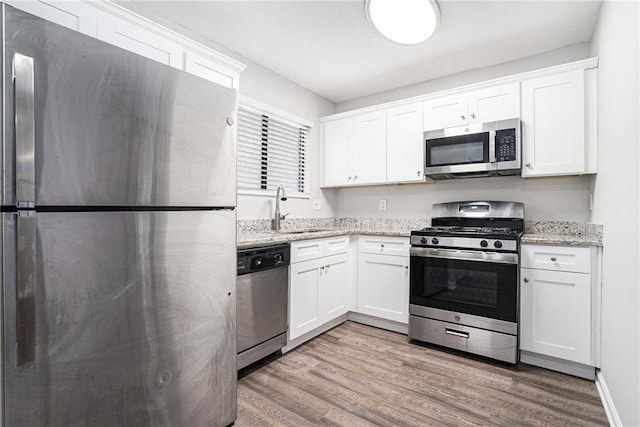 kitchen with light stone countertops, white cabinetry, sink, and stainless steel appliances