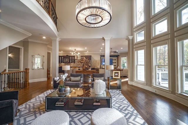 living room featuring crown molding, decorative columns, a high ceiling, wood finished floors, and a notable chandelier