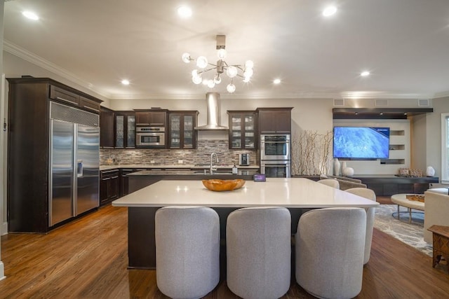 kitchen with dark brown cabinets, stainless steel appliances, wall chimney range hood, and a sink