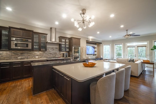 kitchen with a large island with sink, a sink, open floor plan, wall chimney exhaust hood, and tasteful backsplash