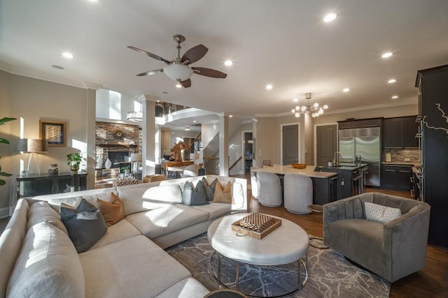 living area with ceiling fan with notable chandelier, decorative columns, ornamental molding, and dark wood-style flooring