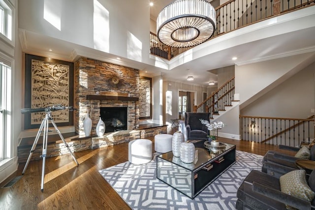 living room featuring crown molding, stairs, a stone fireplace, a high ceiling, and wood finished floors