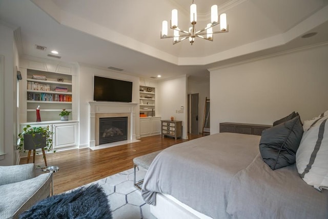 bedroom featuring wood finished floors, visible vents, a fireplace with flush hearth, a raised ceiling, and a chandelier