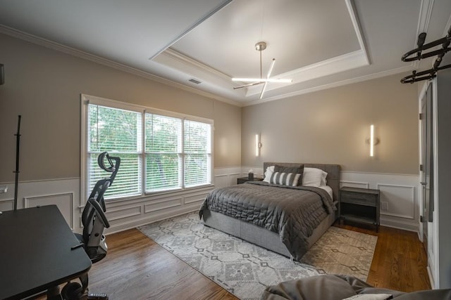 bedroom featuring visible vents, a tray ceiling, wood finished floors, an inviting chandelier, and wainscoting