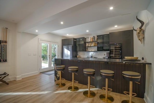 kitchen with baseboards, light wood-style flooring, recessed lighting, a kitchen bar, and stainless steel fridge