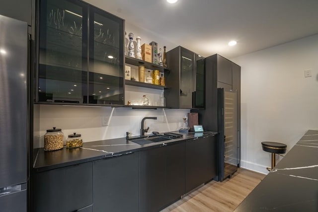 kitchen featuring dark countertops, light wood-style floors, freestanding refrigerator, and a sink