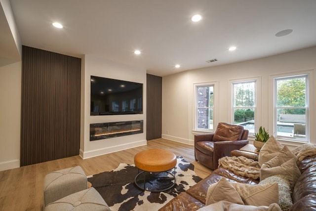 living room featuring light wood finished floors, visible vents, recessed lighting, and a glass covered fireplace