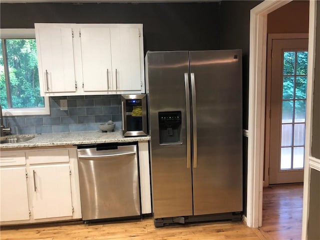 kitchen featuring a sink, tasteful backsplash, white cabinetry, light wood-style floors, and appliances with stainless steel finishes