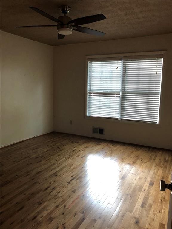 empty room featuring hardwood / wood-style flooring, visible vents, and ceiling fan