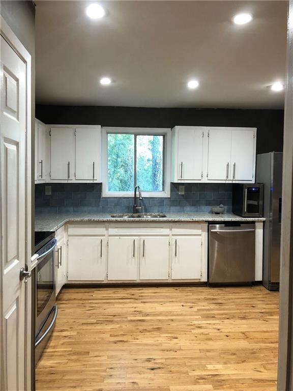 kitchen with light wood-style flooring, a sink, stainless steel appliances, white cabinets, and tasteful backsplash