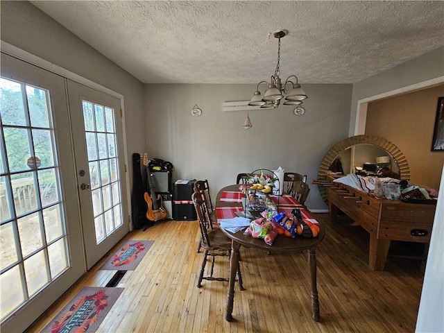 dining space with french doors, light wood-style floors, a chandelier, and a textured ceiling