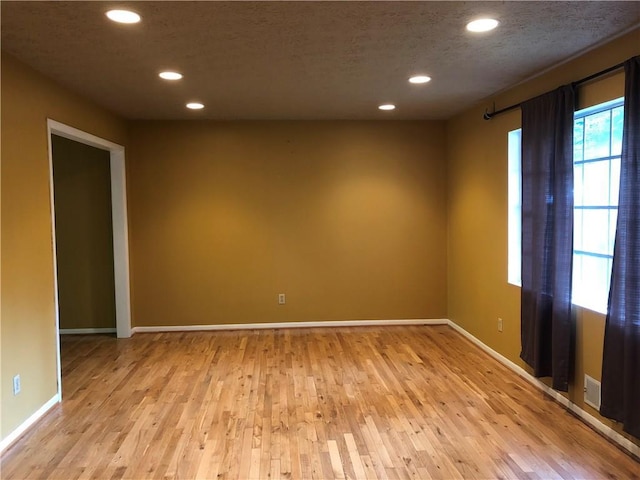 spare room with baseboards, recessed lighting, light wood-type flooring, and a textured ceiling