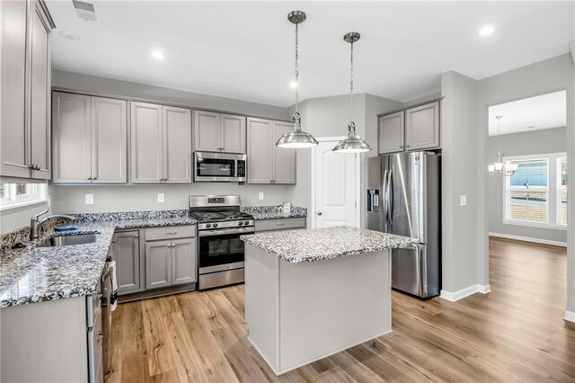 kitchen with gray cabinetry, a kitchen island, stainless steel appliances, and decorative light fixtures