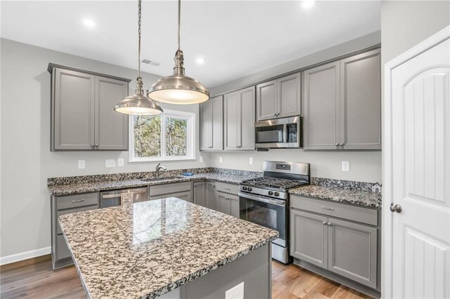 kitchen with gray cabinetry, light stone countertops, stainless steel appliances, and hanging light fixtures