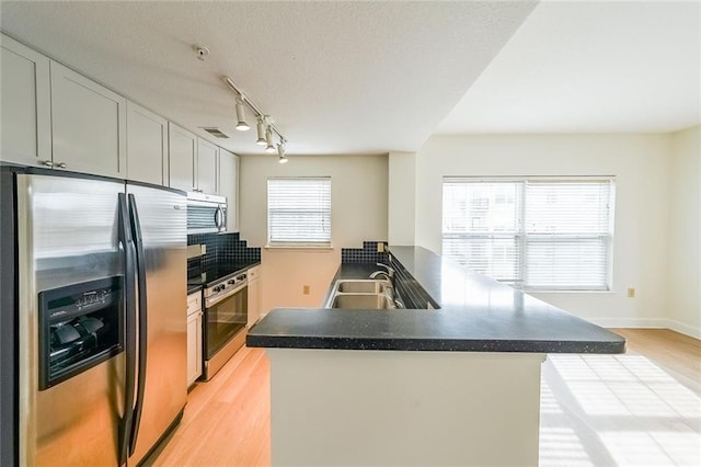 kitchen with sink, light hardwood / wood-style flooring, appliances with stainless steel finishes, plenty of natural light, and kitchen peninsula