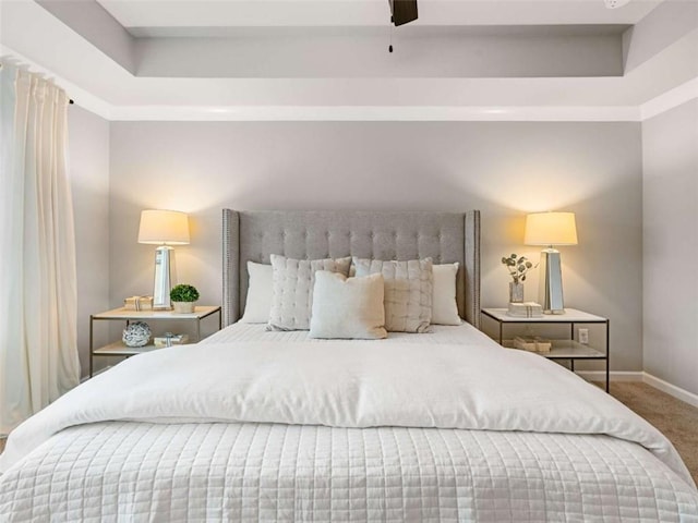 bedroom featuring ceiling fan, a tray ceiling, and carpet