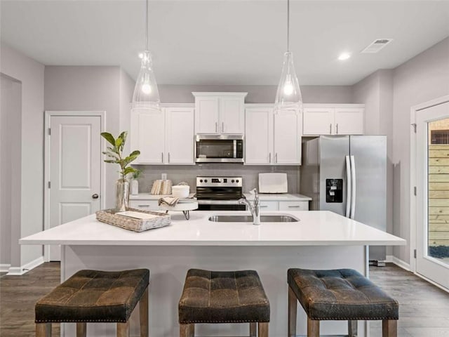 kitchen featuring stainless steel appliances, hanging light fixtures, sink, and a kitchen island with sink