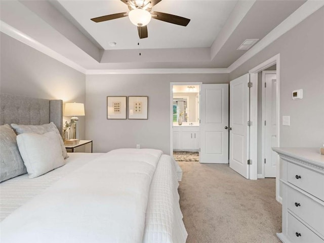 bedroom featuring light carpet, a tray ceiling, ceiling fan, and ensuite bathroom