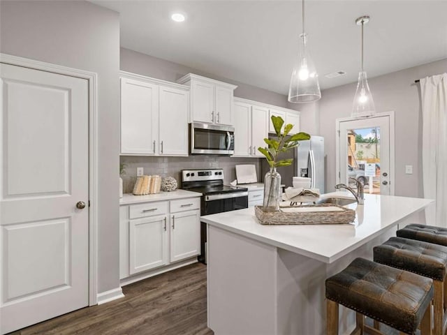 kitchen featuring hanging light fixtures, white cabinetry, appliances with stainless steel finishes, and a center island with sink