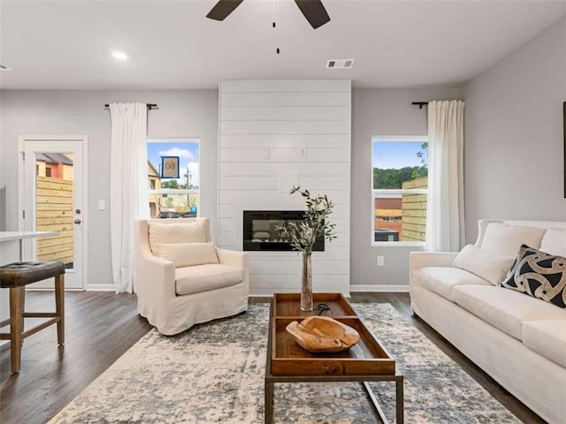 living room featuring ceiling fan, dark wood-type flooring, and a fireplace