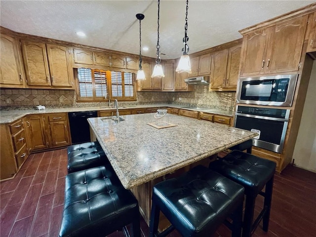 kitchen with an island with sink, black appliances, under cabinet range hood, and a breakfast bar