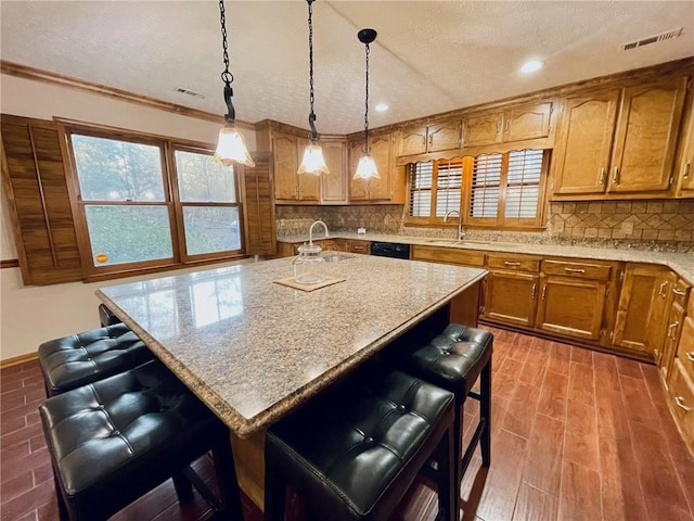 kitchen with brown cabinets, decorative light fixtures, a breakfast bar area, a kitchen island with sink, and a sink